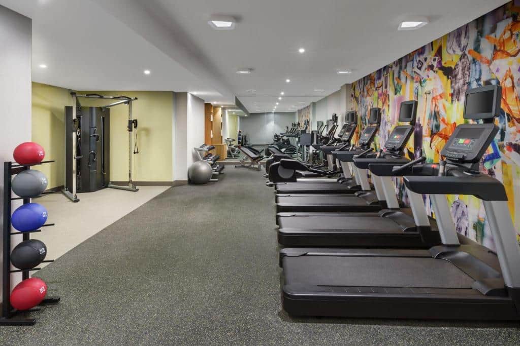 No ginásio do TownePlace Suites by Marriott New York Manhattan Chelsea há uma fila de passadeiras à direita e, à esquerda, uma zona com pesos e uma máquina de musculação. Ao fundo, um grande espelho a cobrir a parede.