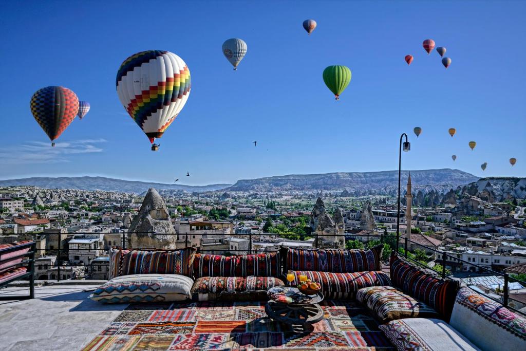 Balões de ar quente coloridos sobre uma localidade com formações rochosas, vistos de um terraço com almofadas e tapetes estampados, no Arinna Cappadocia.