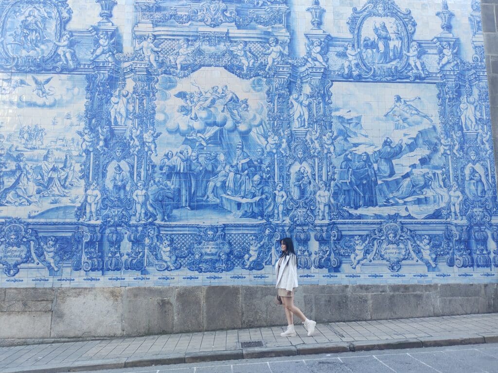 Mulher a passear durante o dia, com o painel de azulejos da Capela das Almas ao fundo.