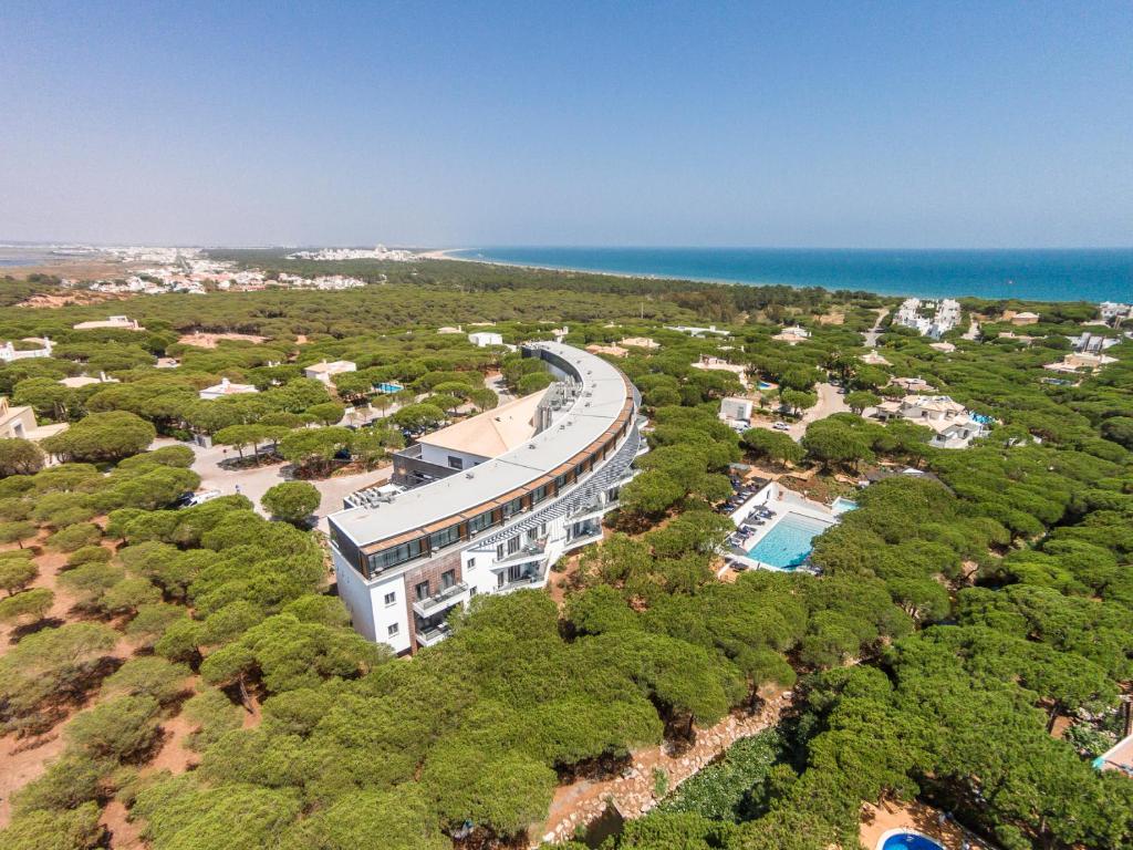 Um edifício curvo, propriedade do Praia Verde Boutique Hotel, na Praia Verde, rodeado de árvores frondosas, com uma piscina e o litoral visível ao fundo.