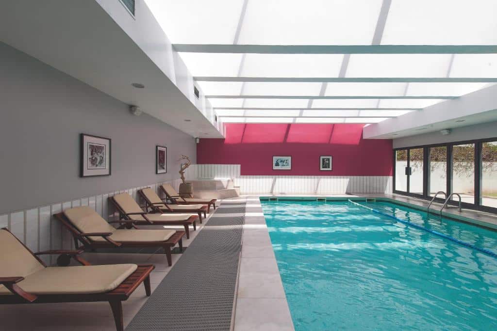 Piscina interior do Vila Gale Opera com espreguiçadeiras, parede rosa e grandes janelas com luz natural
