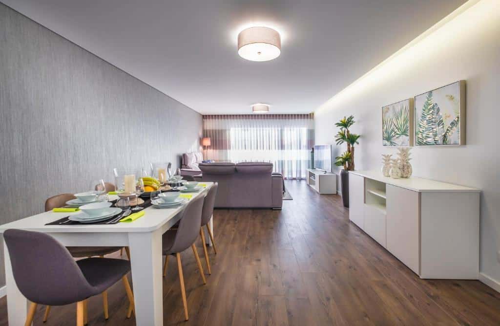 Sala de estar e jantar moderna em espaço aberto, com soalho em madeira, decoração neutra e grandes janelas com cortinados transparentes, no Alto das Nogueiras House Fátima.