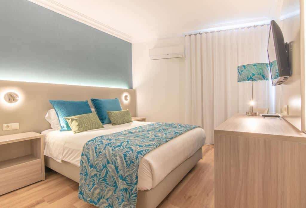 Um quarto moderno no Loulé Jardim Hotel em Loulé, com uma cama de casal, decoração azul e verde, uma TV na parede e móveis de madeira clara.