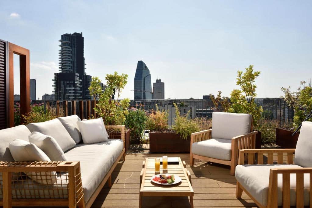 Terraço na cobertura do Milano Verticale | UNA Esperienze com poltronas e um sofá estofados com vista para a cidade e vasos de plantas