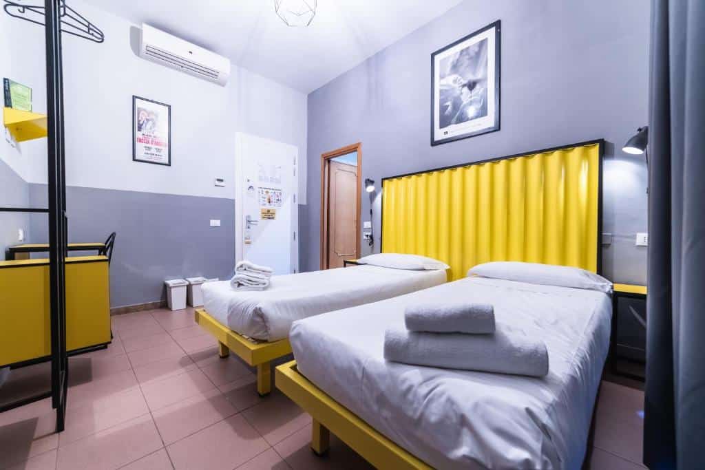 quarto do hostel YellowSquare Rome com duas camas de solteiro e pormenores em amarelo, decoração de estilo industrial, ar condicionado e arara para roupa
