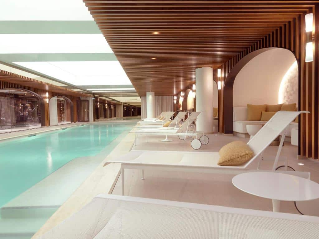 Zona da piscina interior do Hôtel D’Aubusson com espreguiçadeiras modernas, painéis de madeira no teto, iluminação suave e almofadas decorativas ao longo da lateral. Este é um dos hotéis de luxo em Paris.