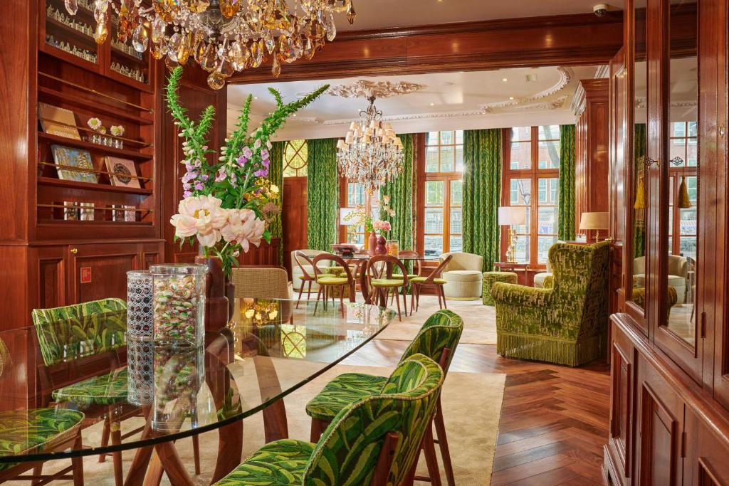 Sala de jantar e sala de estar do Hotel Estheréa, com painéis de madeira, cadeiras com padrão verde, lustres e janelas grandes com cortinados verdes.