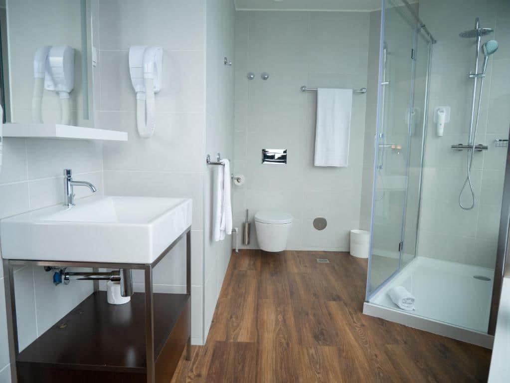 Casa de banho do easyHotel Lisbon, com um chuveiro do lado direito, um lavatório com móvel por baixo, um espelho e toalhas brancas penduradas.