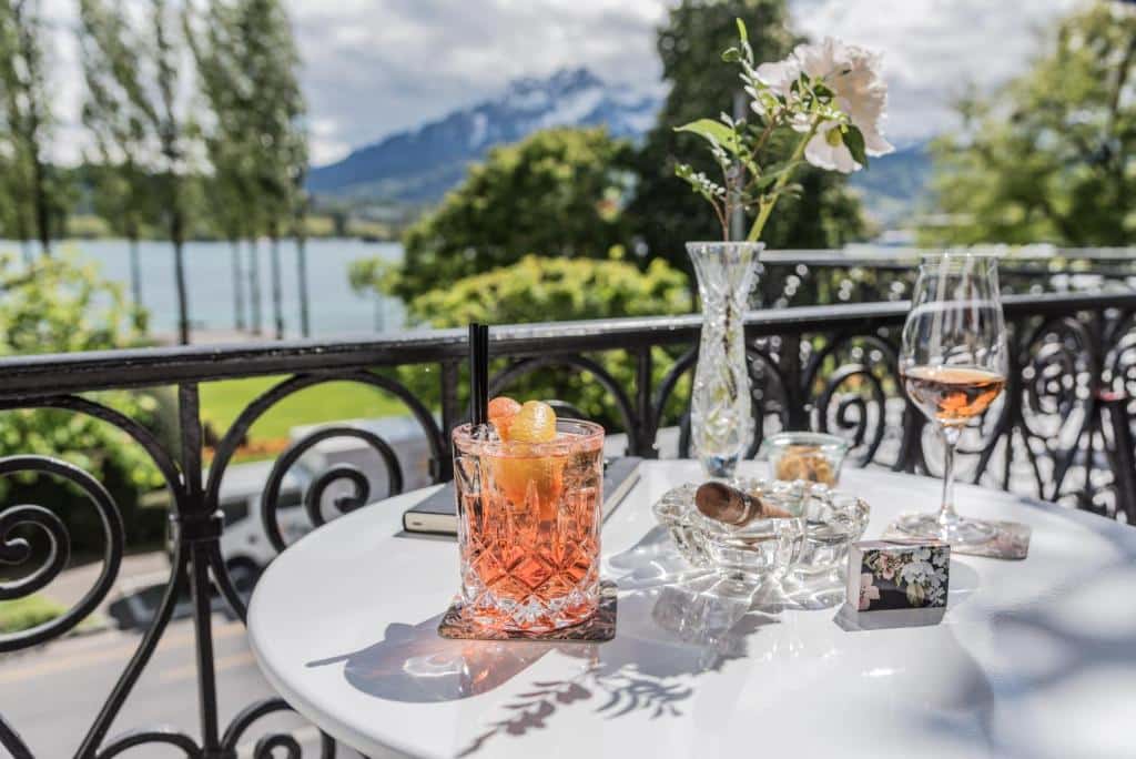 Varanda do Hotel Beau Séjour, com mesa e vista para árvores, lago e montanhas.