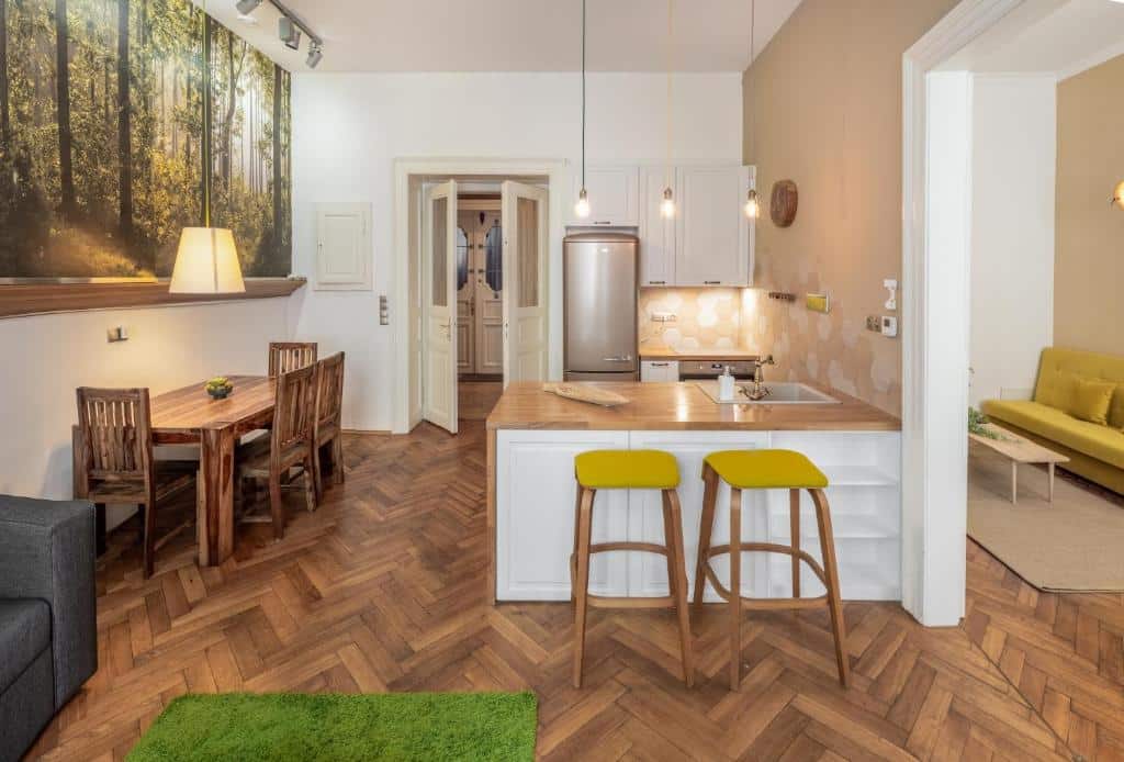 Apartamento do Mordecai 12 Apartments, com cozinha aberta e zona de refeições com chão de madeira, bancos de bar e uma mesa de jantar.