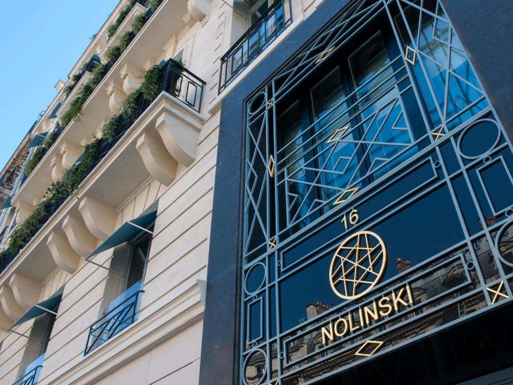 A entrada de um edifício chamado “Nolinski Paris” com janelas grandes, desenhos geométricos e o número 16 por cima da porta. Este é um dos hotéis de luxo em Paris.