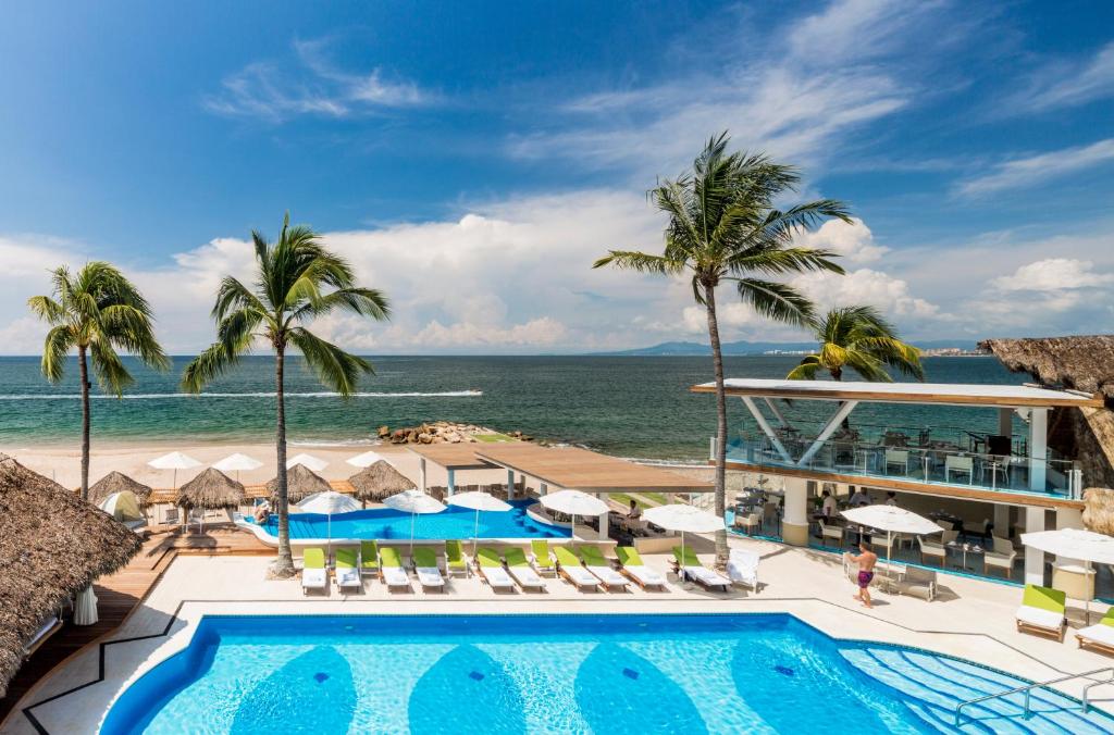 Vista do Villa Premiere Boutique Hotel à beira-mar com piscina, palmeiras, espreguiçadeiras, chapéus de sol e o oceano ao fundo.