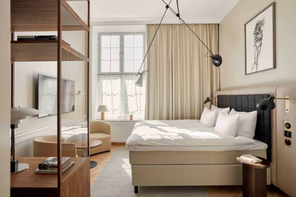 Quarto do hotel Villa Copenhagen com cama de casal, estante, mesa pequena, duas poltronas, candeeiros e uma janela.