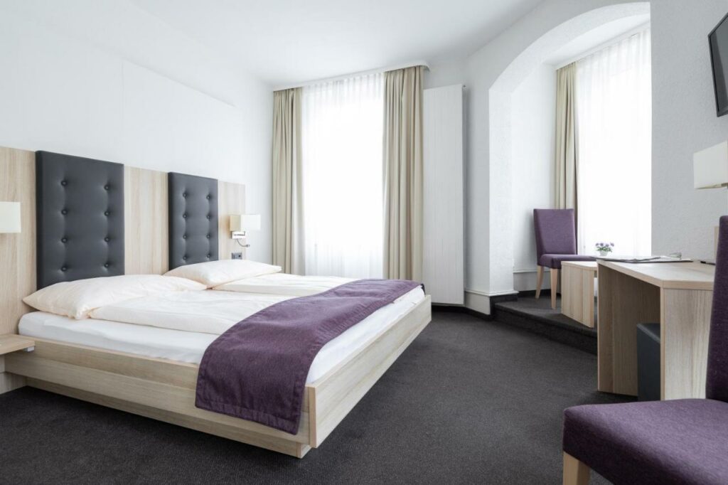Quarto do Hotel Lötschberg com cama de casal, secretária e poltrona.