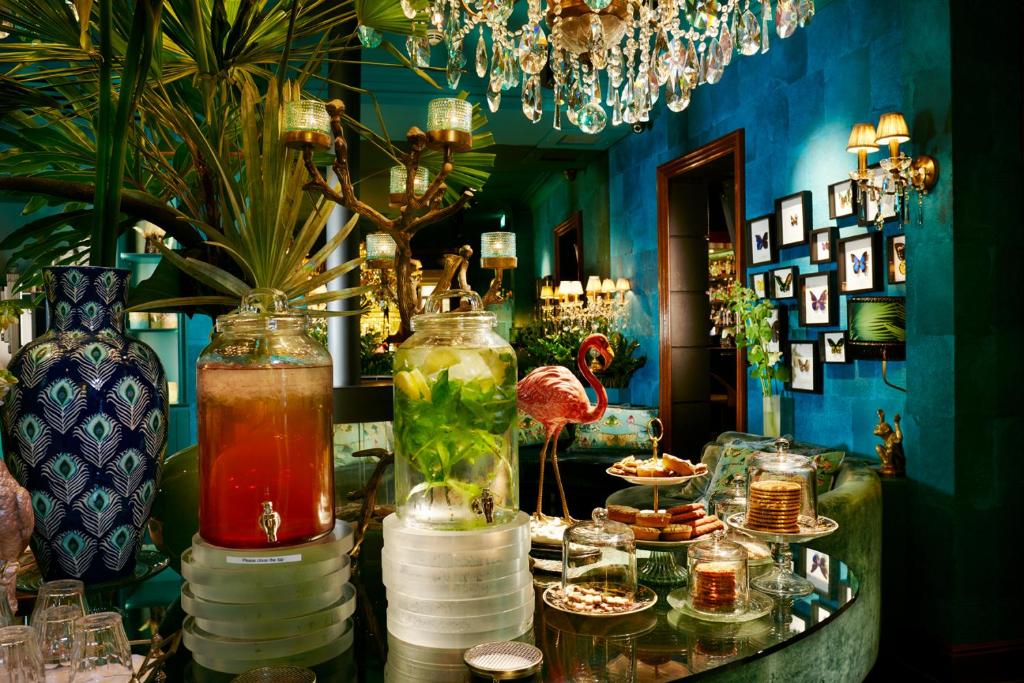 Mesa de vidro do Hotel Estheréa com jarros de sumo e alimentos, num ambiente de paredes azul-turquesa, lustre e quadros