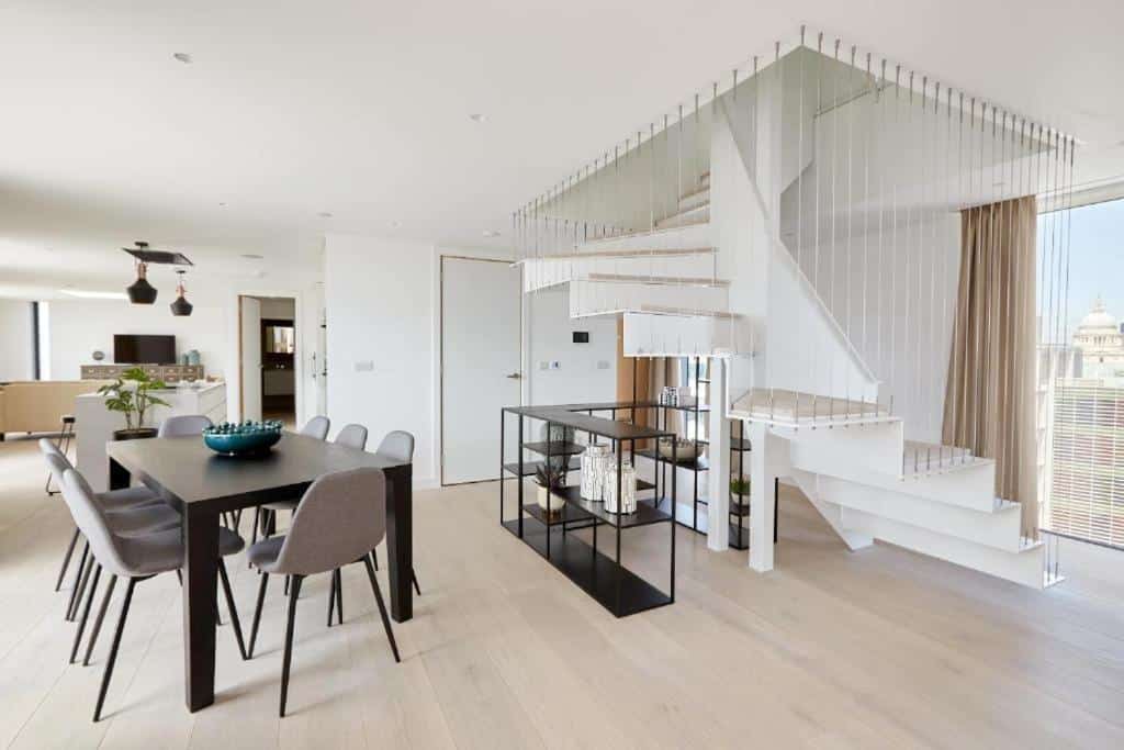 Sala ampla do Southwark by Q Apartments com janela panorâmica, uma escada para o segundo andar, chão de madeira, mesa de refeições de seis lugares e alguns elementos decorativos.