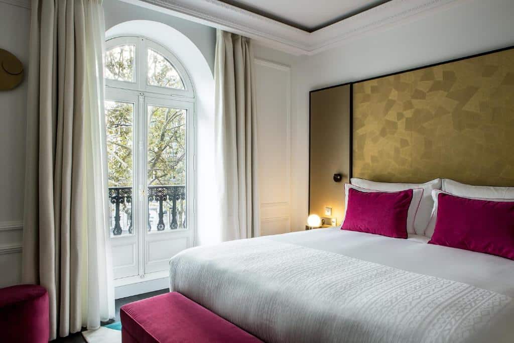 Um quarto do Fauchon L’Hôtel Paris com uma cama grande, lençóis brancos, almofadas magenta e uma janela com cortinas com vista para as árvores.