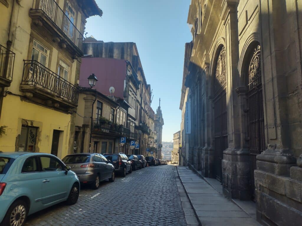Rua da cidade do Porto durante o dia, com carros do lado esquerdo da imagem e casas em redor.
