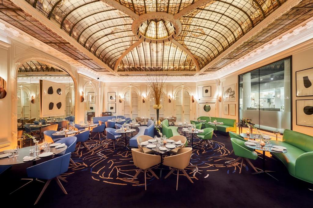 Restaurante elegante do Hôtel Vernet Champs Elysées Paris com um grande teto de vidro colorido, mobiliário moderno, mesas postas e arte contemporânea nas paredes. Este é um dos hotéis de luxo em Paris.