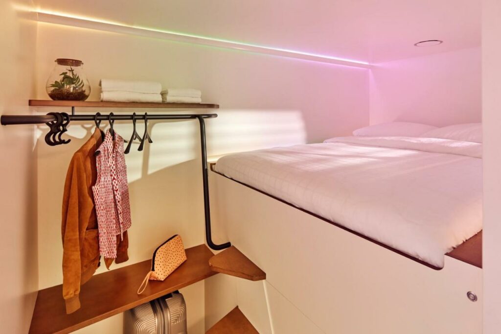 Quarto-cabine do CityHub Copenhagen com uma cama de casal mais alta, duas prateleiras e um bengaleiro com roupa.