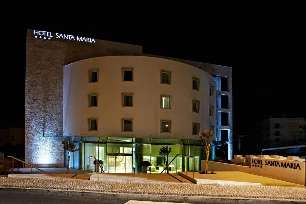 Hotel Santa Maria à noite, com exterior iluminado, entrada de vidro e sinalização visível do hotel no edifício.