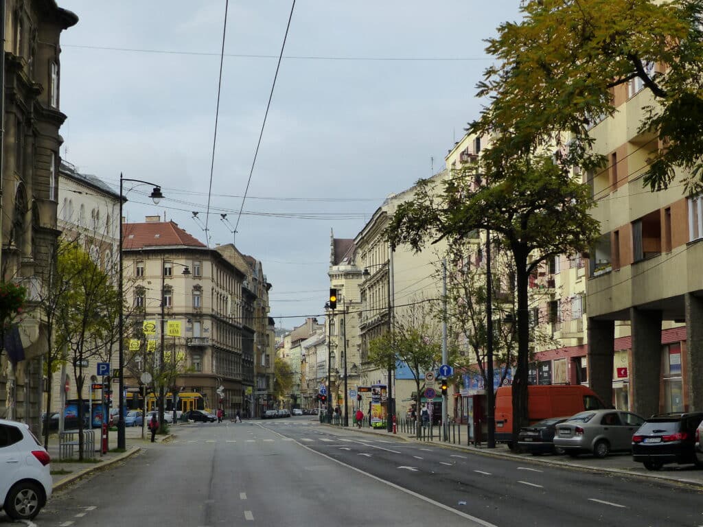 Uma rua tranquila em Józsefváros, com carros estacionados dos dois lados, ladeada por árvores e prédios de apartamentos, num dia nublado.