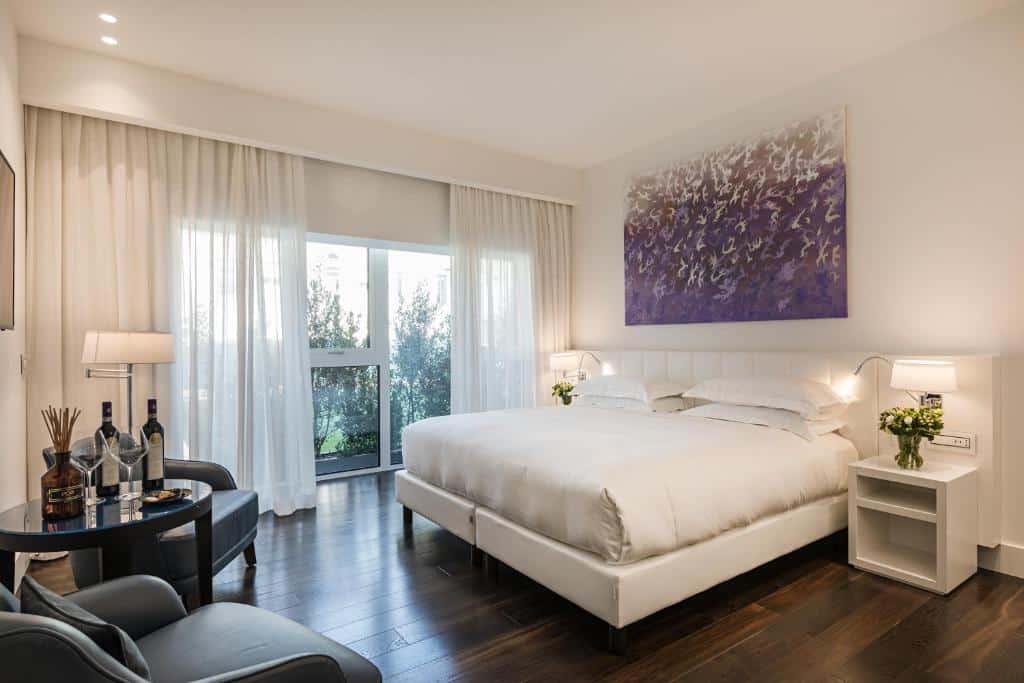 Quarto amplo e delicado com cama de casal, mesa e cadeira e janela de parede inteira no Magna Pars l'Hotel à Parfum