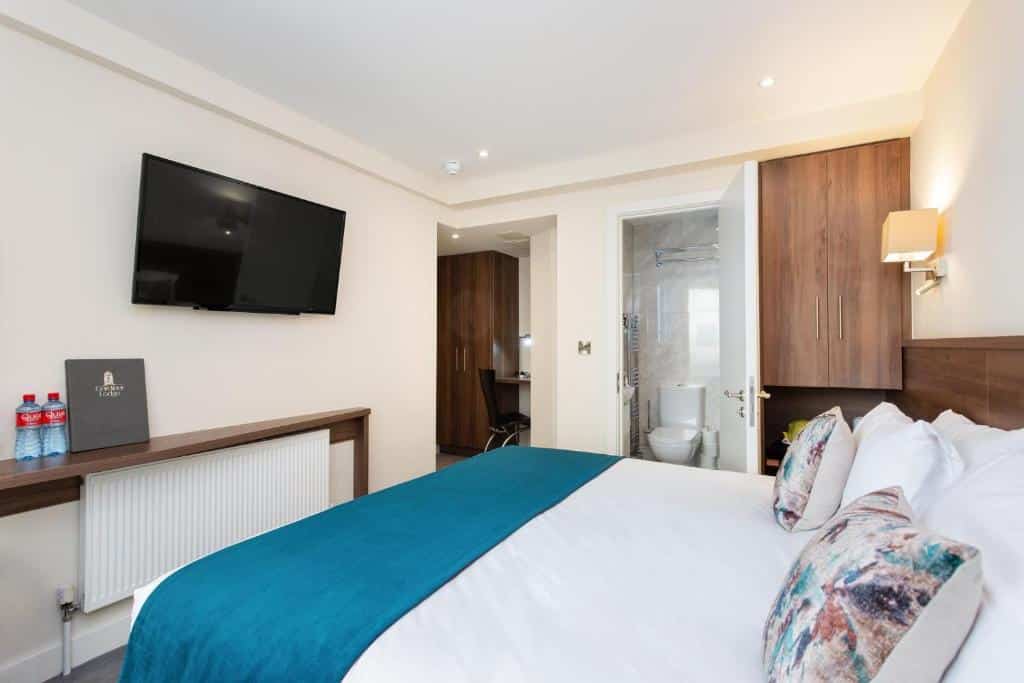 Quarto do Gardiner Lodge com mobiliário de madeira e casa de banho contígua, televisão de ecrã grande na parede e garrafas de água no chão.