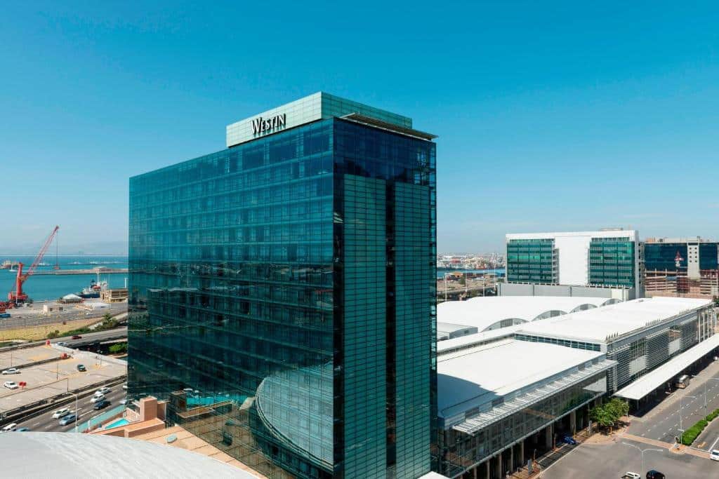 O hotel The Westin Cape Town junto a um centro de congressos no centro da Cidade do Cabo, com o porto e prédios ao fundo.