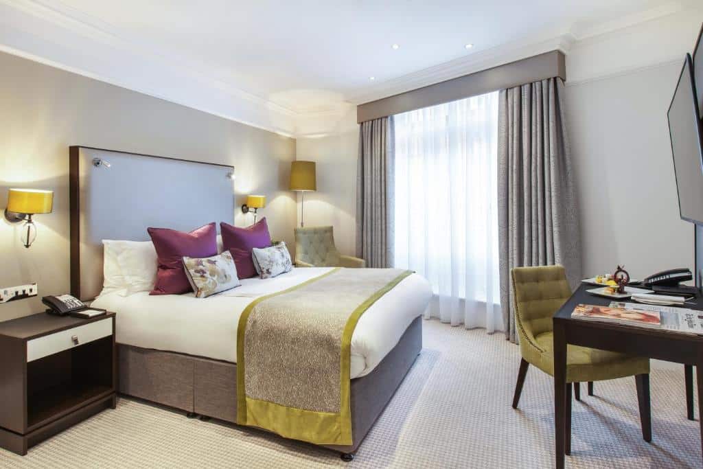 Quarto do St. James’ Court, A Taj Hotel, London com janela com cortinas, cama de casal, mesa com poltrona, televisão e mesas de cabeceira com candeeiros