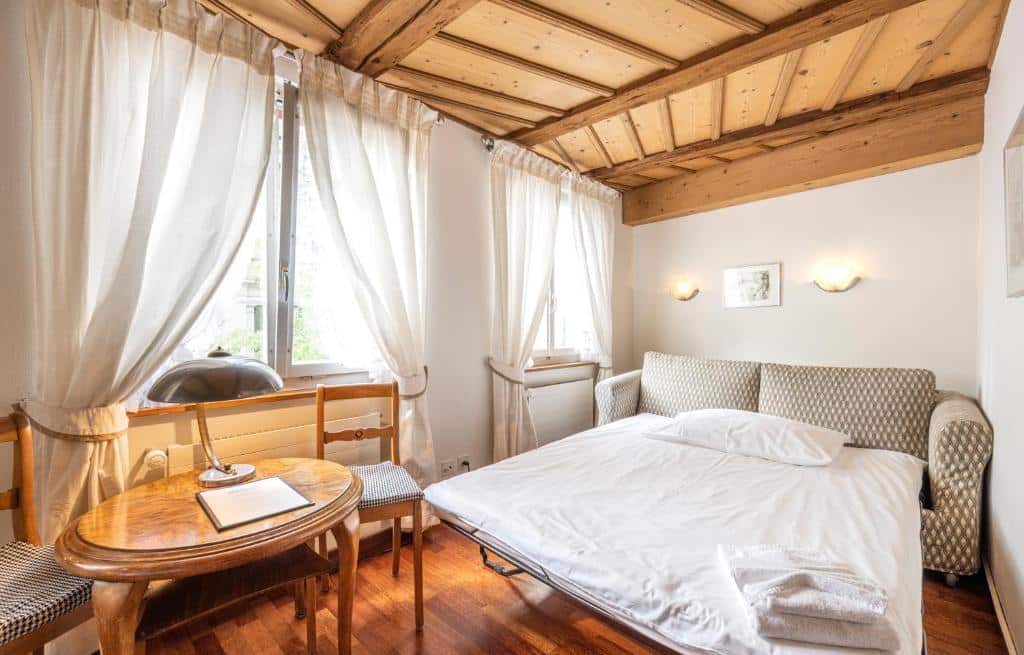 Quarto do Hotel Rebstock, em Lucerna, com sofá-cama, mesa de madeira e duas janelas.