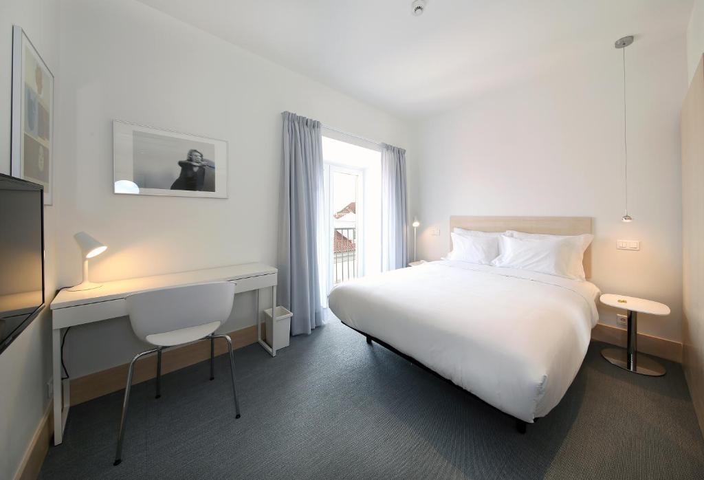 Quarto do Hotel Convento do Salvador com uma cama de casal, uma pequena varanda com cortinas, uma secretária com cadeira e uma televisão.