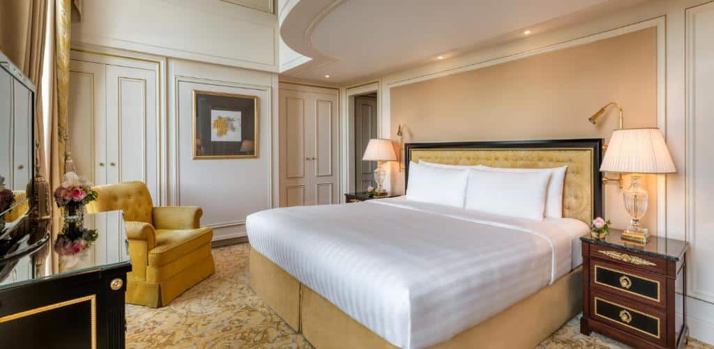 Um quarto do Shangri-La Paris com uma cama grande, poltrona amarela, duas mesas de cabeceira com luminárias e um quadro emoldurado na parede.