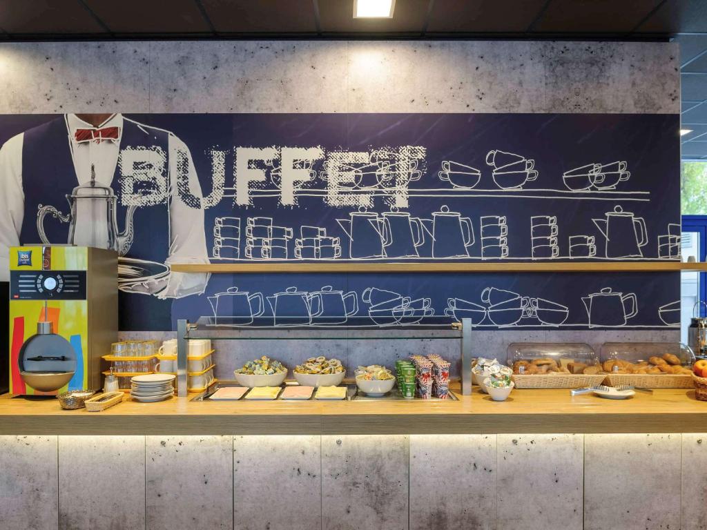 Buffet de pequeno-almoço no Ibis budget Wien Sankt Marx, com doces, cereais, condimentos e uma máquina de bebidas quentes num balcão de madeira.