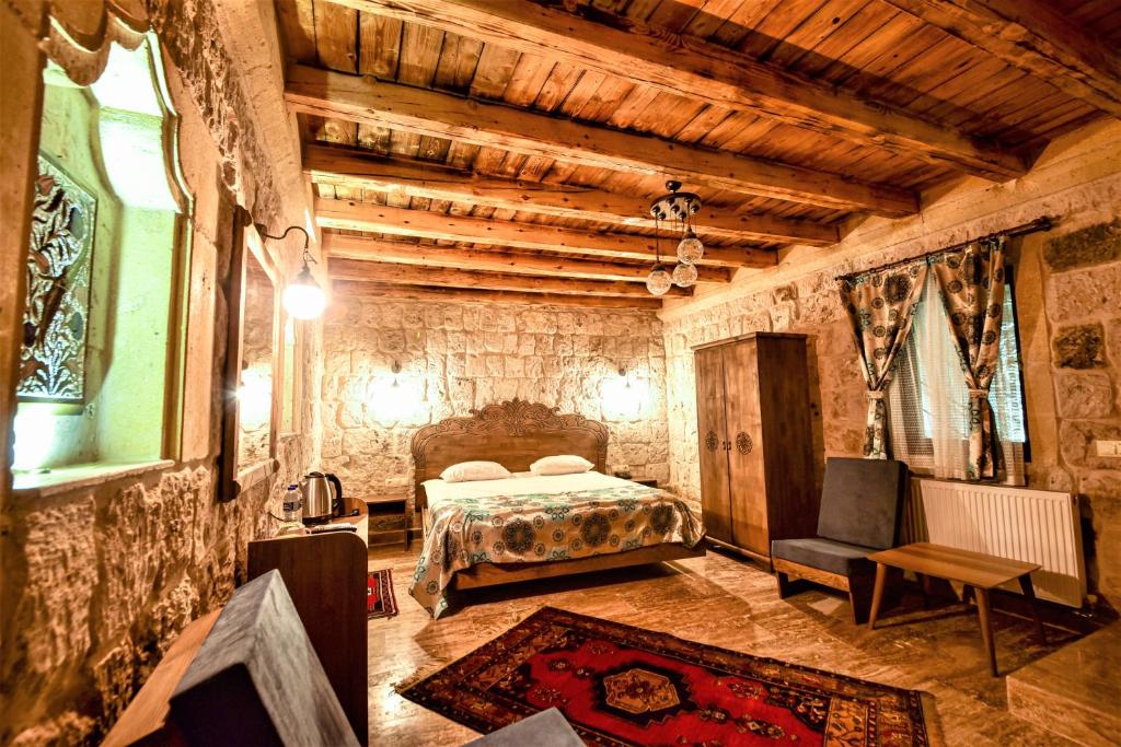 Quarto rústico do Cappadocia Caves Hotel, um dos hotéis da Capadócia, com paredes de pedra, tecto de madeira, cama de casal, roupeiro, cadeiras, tapete e cortinados estampados.