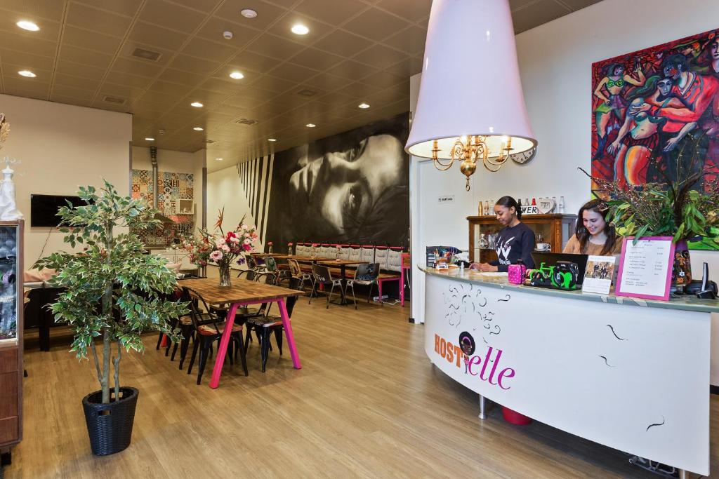 Receção do Hostelle, um hostel só para mulheres em Amesterdão, com um balcão e duas mulheres a sorrir, e ao fundo mesas, cadeiras e flores