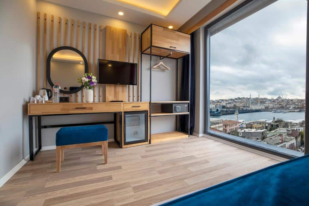 Quarto do Union Hotel Karaköy com toucador, TV, frigorífico, cofre e janela grande com vista para a cidade e a orla.