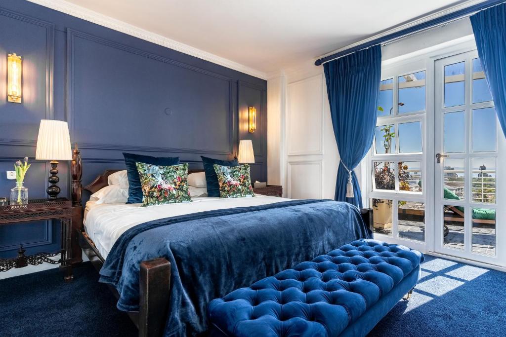 Quarto no Romney Park Luxury Apartments com parede em tons de azul, roupa de cama azul, dois candeeiros e portas de vidro para uma varanda.