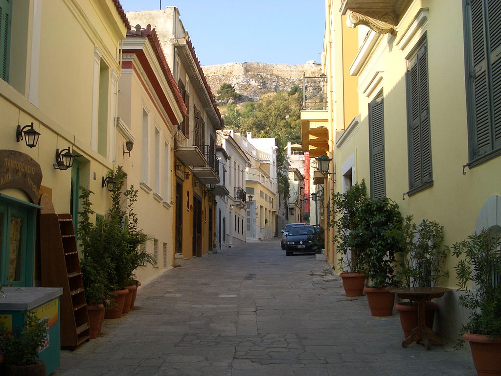 Rua estreita com automóveis estacionados e casinhas coloridas no bairro de Plaka, em Atenas